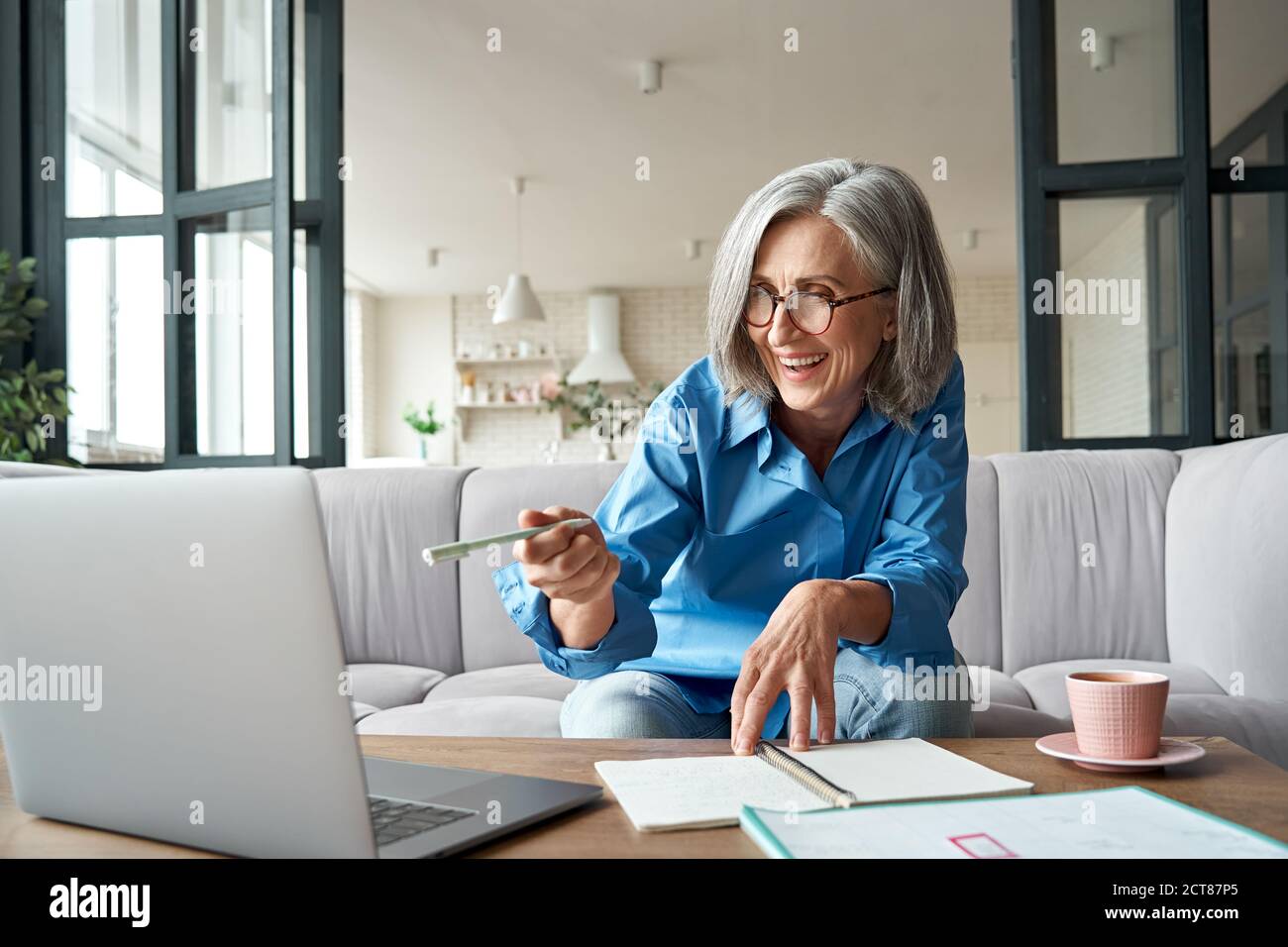 Happy mature older woman video calling on laptop working from home. Stock Photo