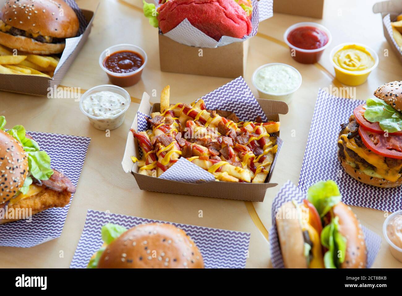 Burger restaurant layout with cheese & bacon loaded fries placed on light wooden surface. Stock Photo