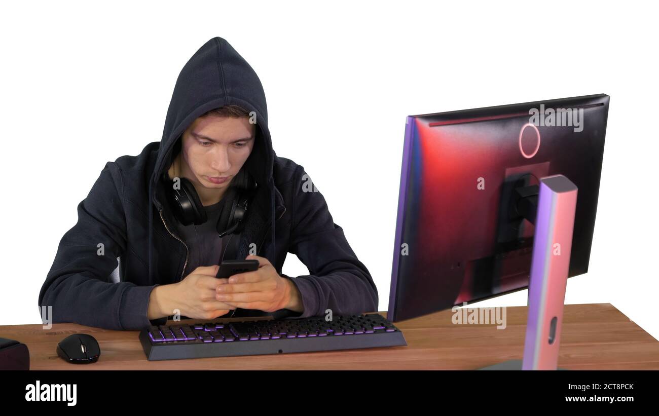 Hooded hacker using laptop and smartphone on white background. Stock Photo