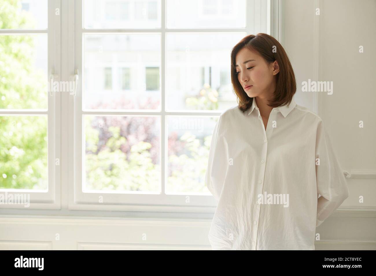 young asian woman standing by window at home looking bored and sad Stock Photo