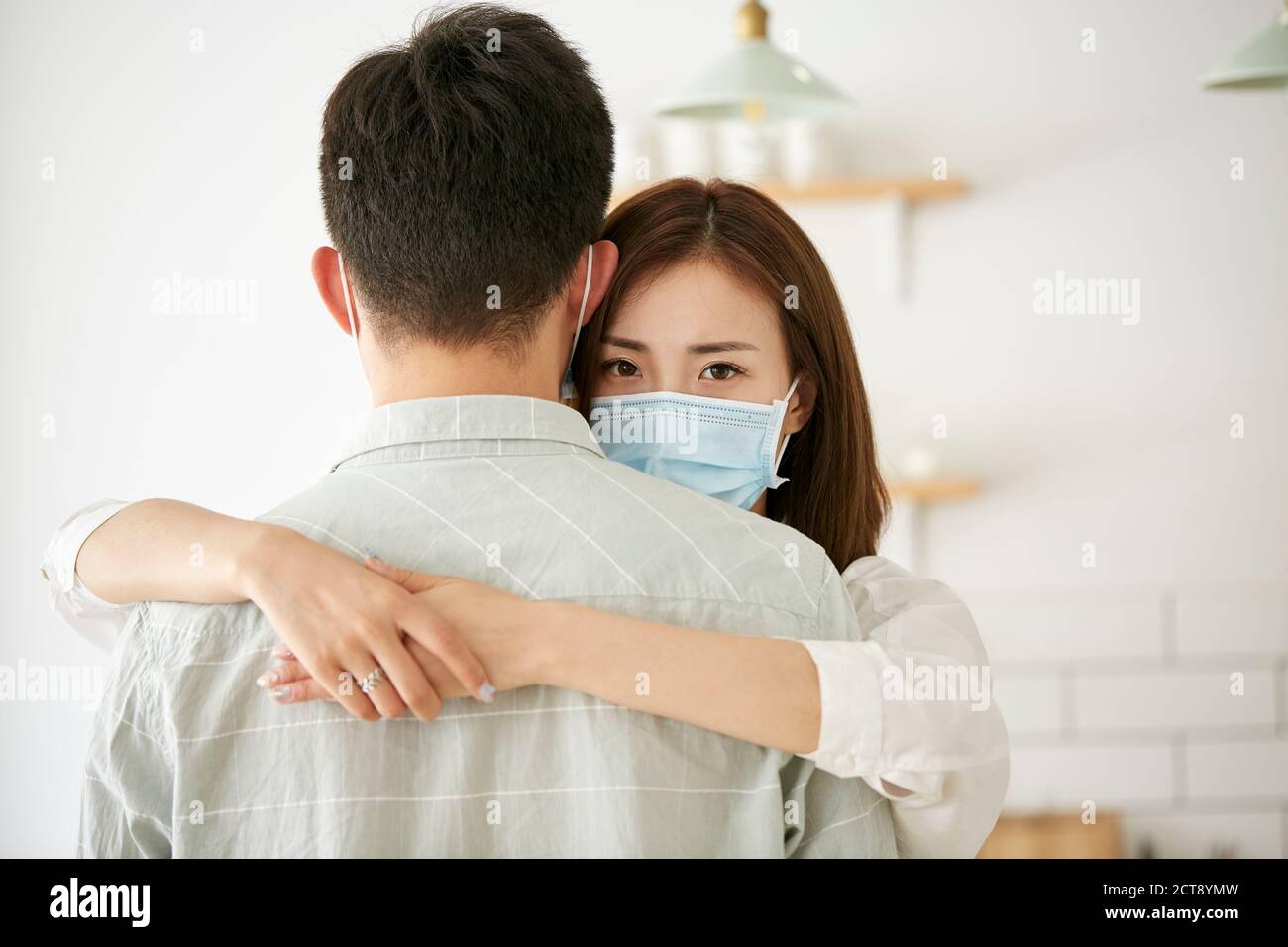 young asian woman wearing mask hugging husband looking at camera Stock Photo