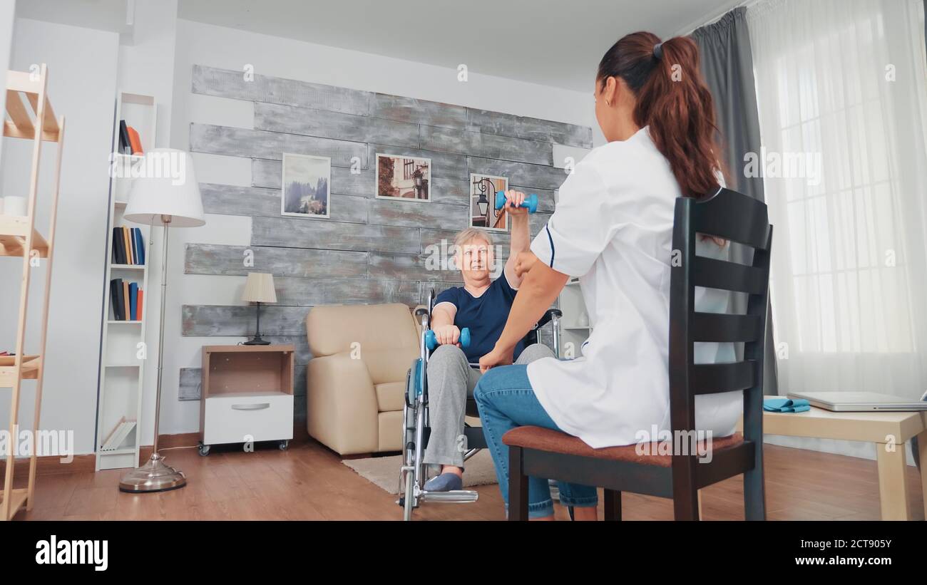 Senior woman in wheelchair doing muscle recovery rehabilitation with nurse. Disabled handicapped old person recovering professional help nurse, nursing retirement home treatment and rehabilitation Stock Photo