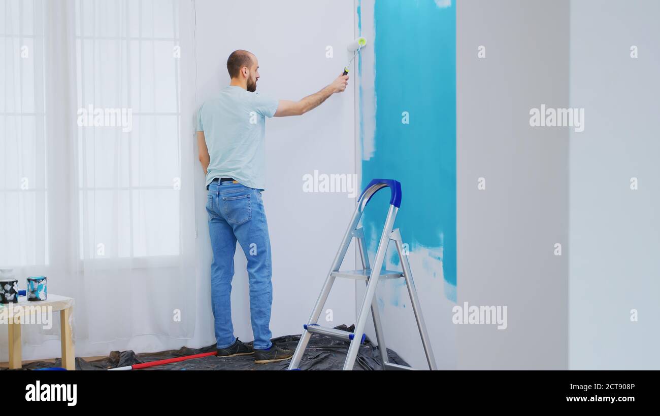 Painting blue wall with white paint using roller brush during home