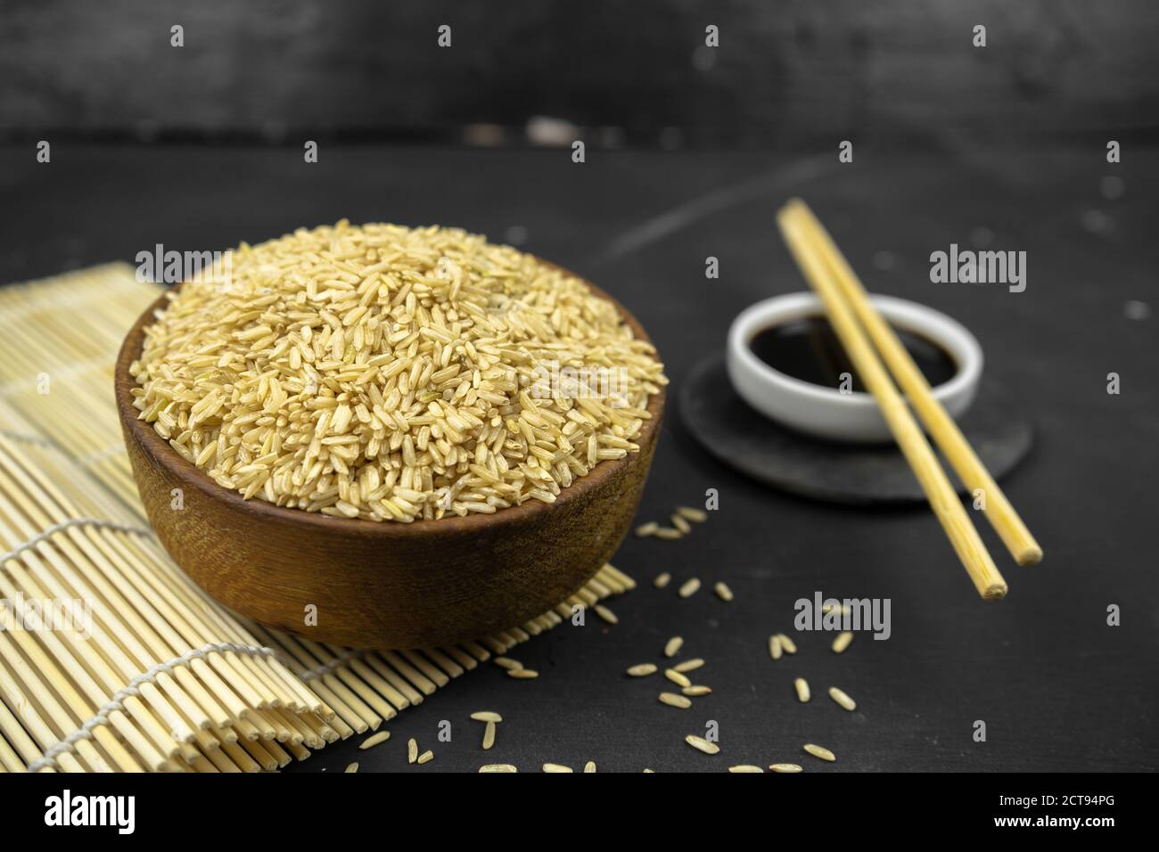 brown rice in a wooden bowl on bamboo mat, asian kitchen background on black Stock Photo