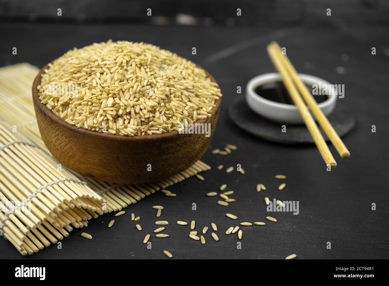 brown rice in a wooden bowl on bamboo mat, asian kitchen background on black Stock Photo