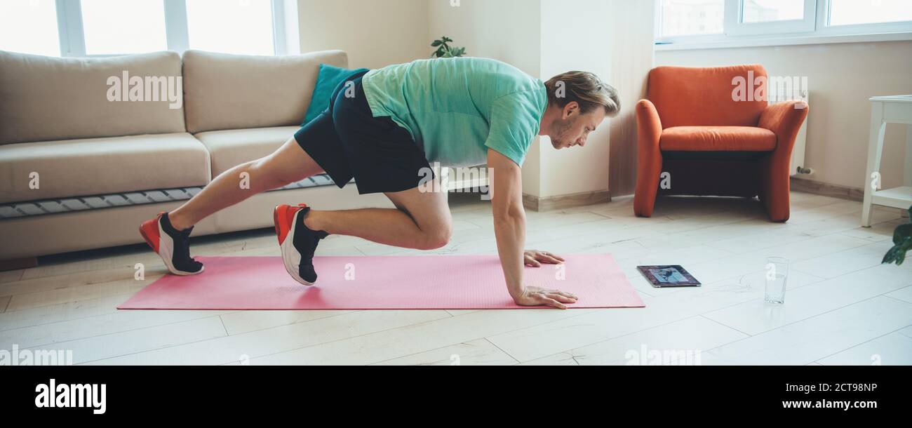 Caucasian man doing fitness exercises at home using a tablet while planking on a carpet Stock Photo