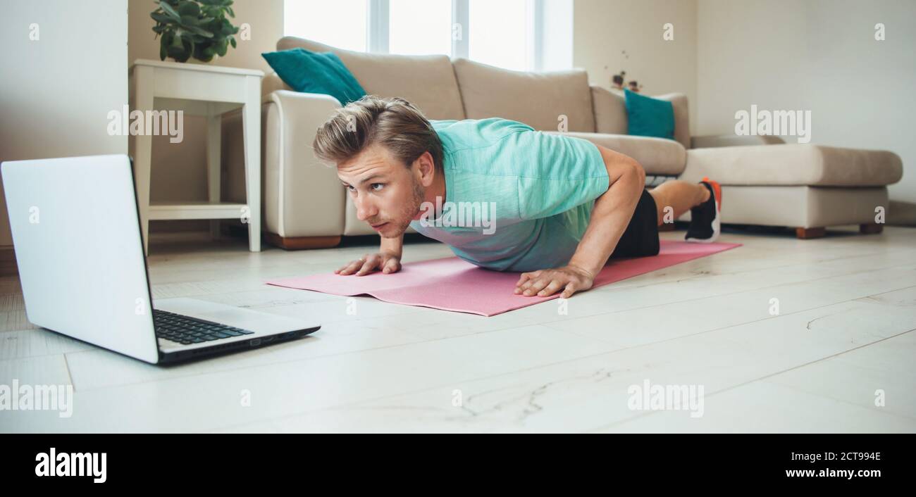 Caucasian man doing push-ups at home on the floor while using a laptop doing home based gym Stock Photo