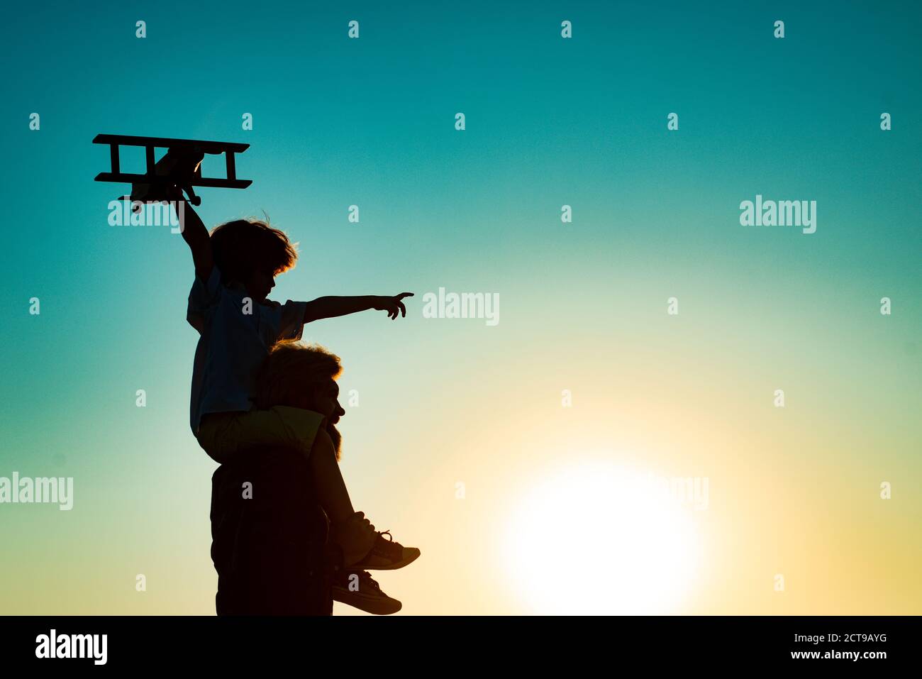 Sunset silhouette of Father carrying his son on shoulders. Child son pilot and dad daddy father with airplane. Stock Photo