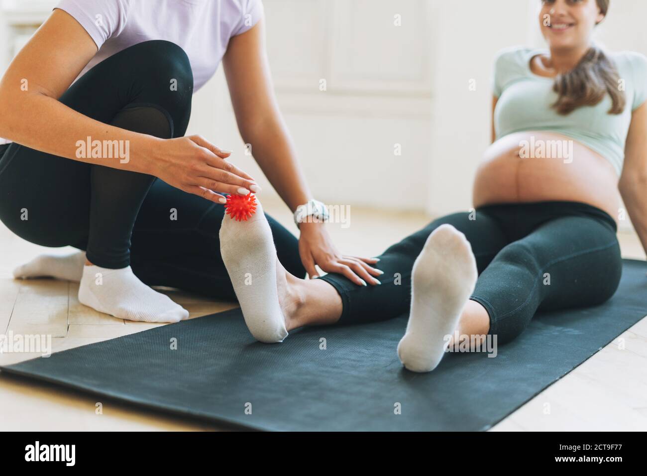 The trainer massages pregnant woman's feet with spiked ball, prevention of flat feet Stock Photo