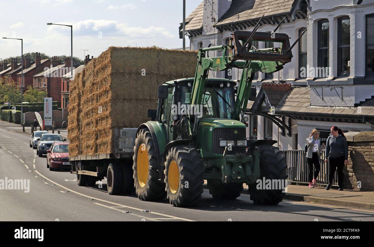 Early autumn in Burscough as straw harvested from the surrounding fields is taken for dry storage by tractor and trailer passed The Packet House pub Stock Photo