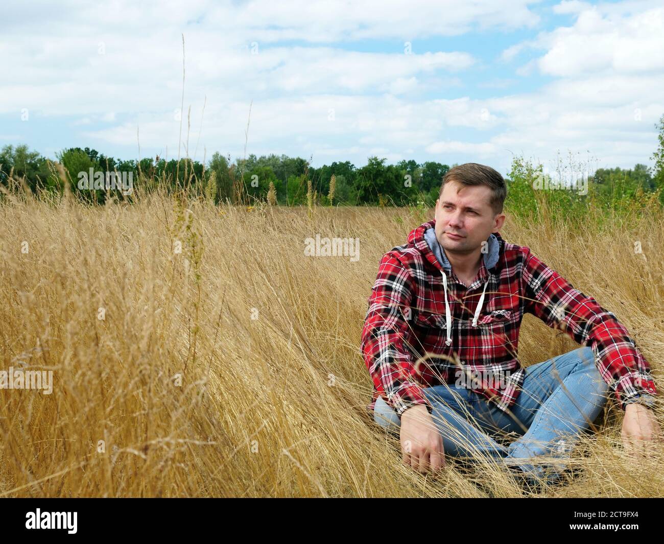 A young guy in a red shirt relaxes and rests in the autumn nature. Stock Photo