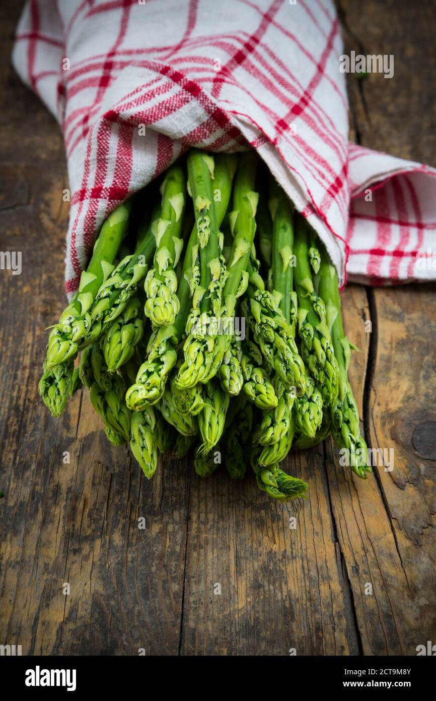 Bunch of green asparagus, Asparagus officinalis, wrapped in kitchen towel lying on dark wood Stock Photo