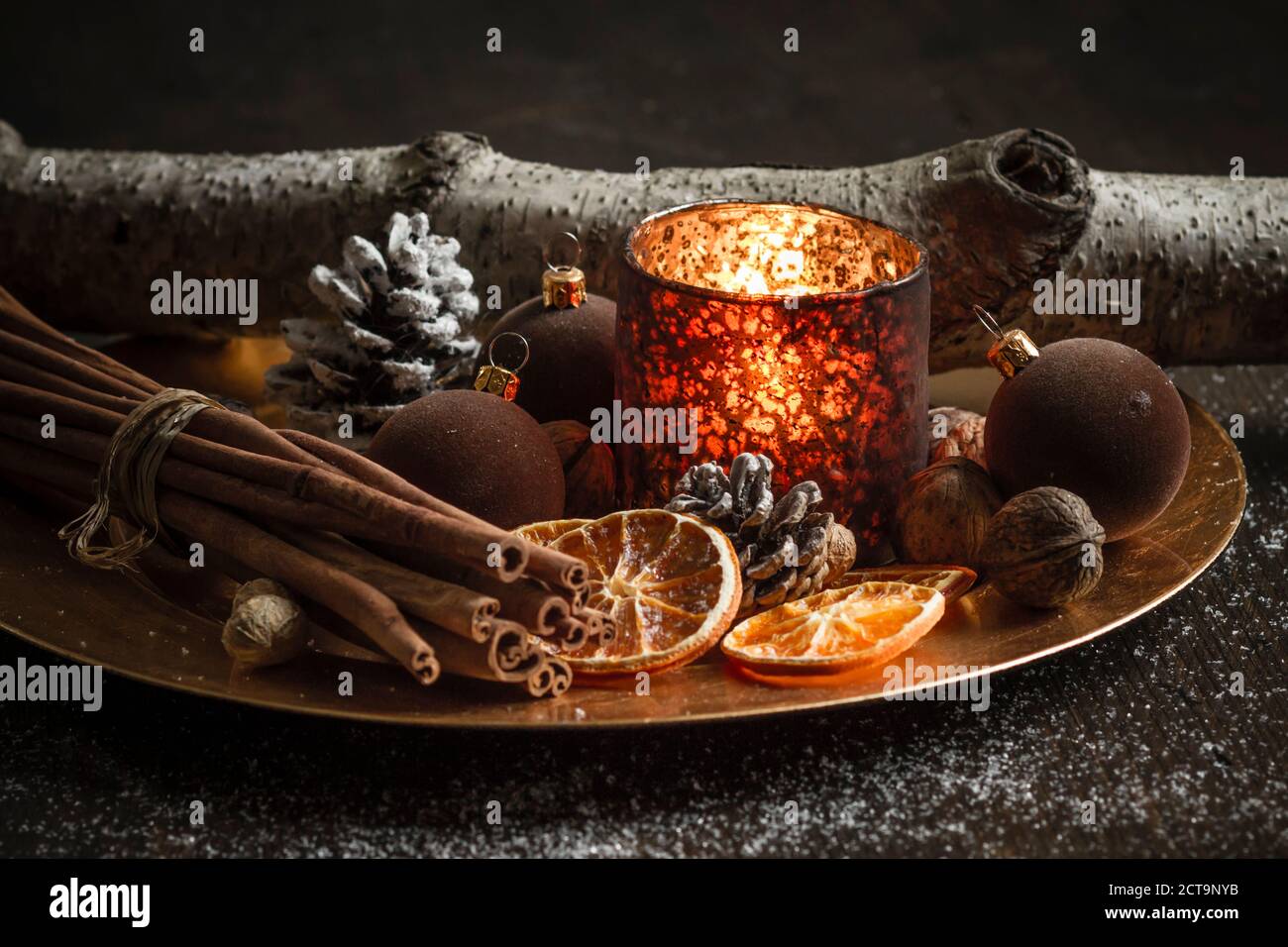 Christmas decoration with tea light candle, christmas tree balls, cinnamon sticks, slices of dried oranges and walnuts on plate, studio shot Stock Photo