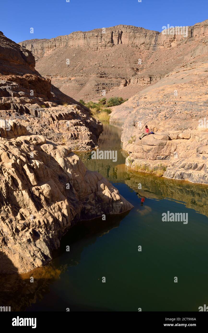 Africa, Algeria, Tassili N'Ajjer National Park, Iherir, Woman resting near water in a guelta, Idaran Canyon Stock Photo