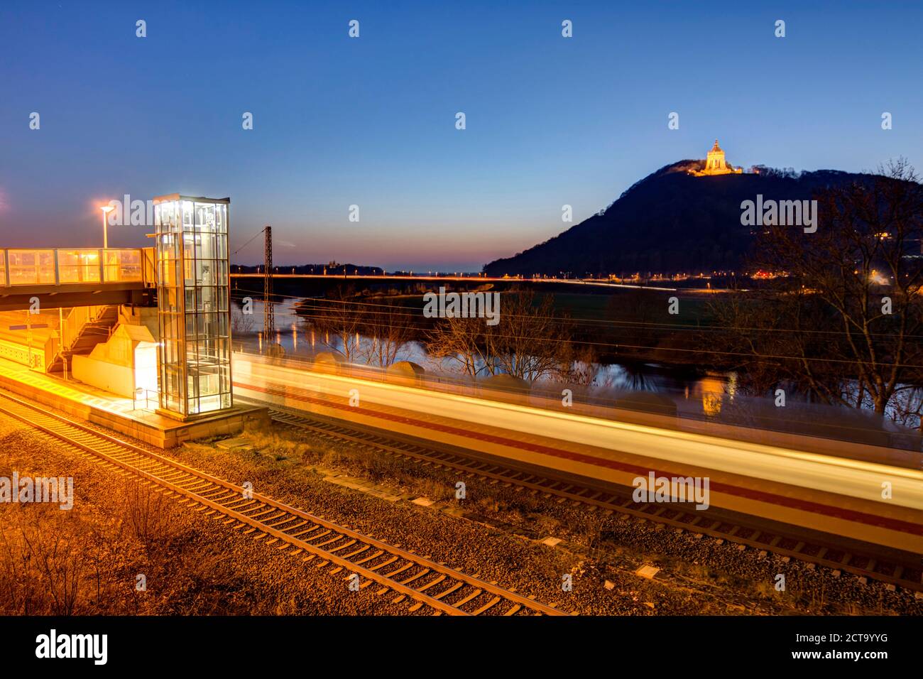 Germany, North Rhine-Westphalia, Porta Westfalica, lighted Emperor-Wilhelm monument at Wiehen hills with platform and railway tracks in front Stock Photo