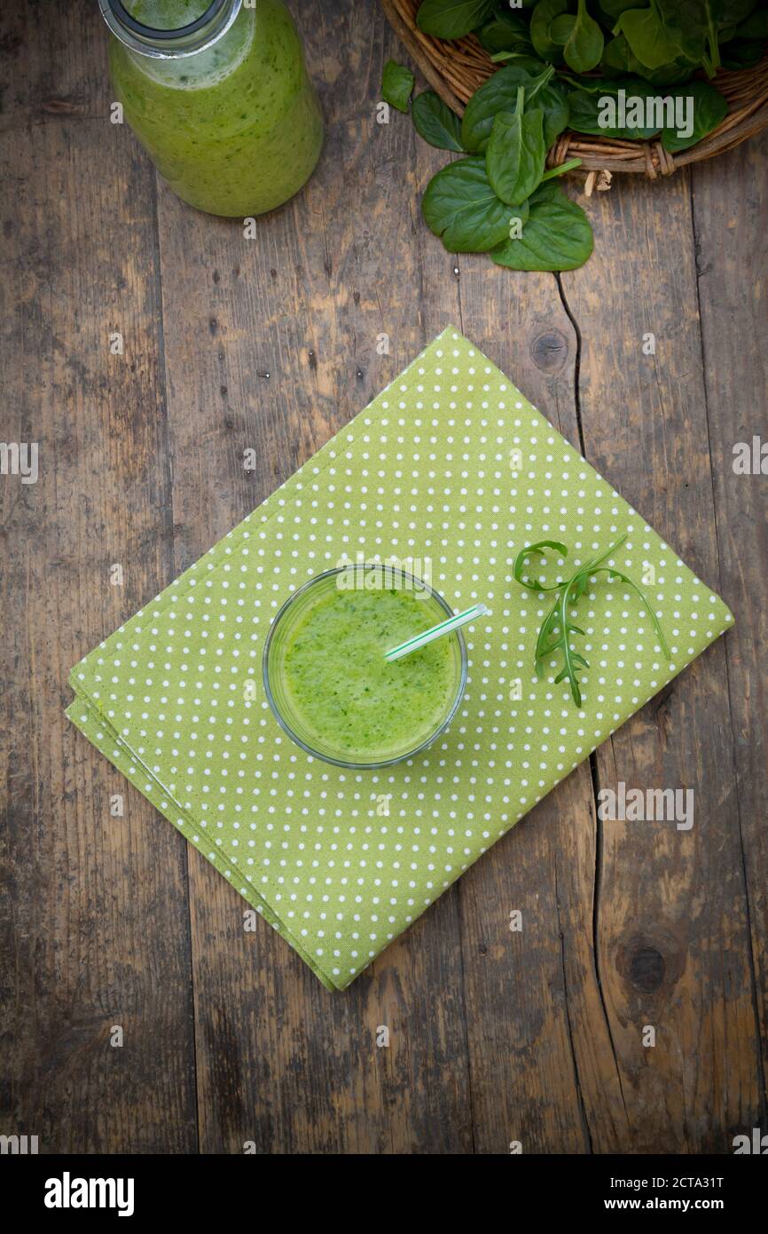 Glass bottle and glass of green smoothie, made of spinach, rocket salad, apple, orange, banana and cucumber, on wooden table, elevated view Stock Photo