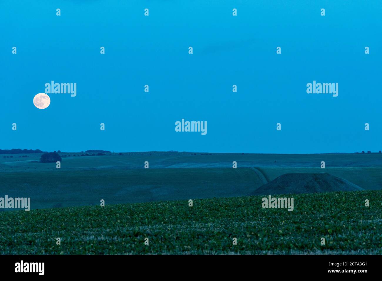 A full moon rises beside the huge Neolithic chalk mound of Silbury Hill, Avebury, Wiltshire, UK. It is 40m high and was built around 2300 BC Stock Photo