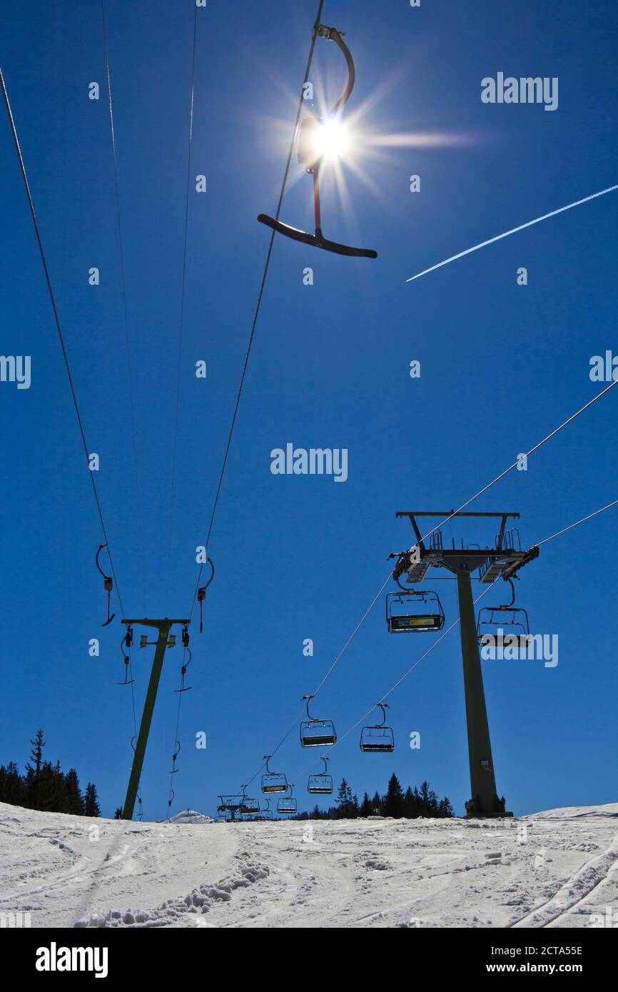 Germany, Bavaria, Winklmoosalm, T-bar lift, chair lift and vapour trail, against the sun Stock Photo