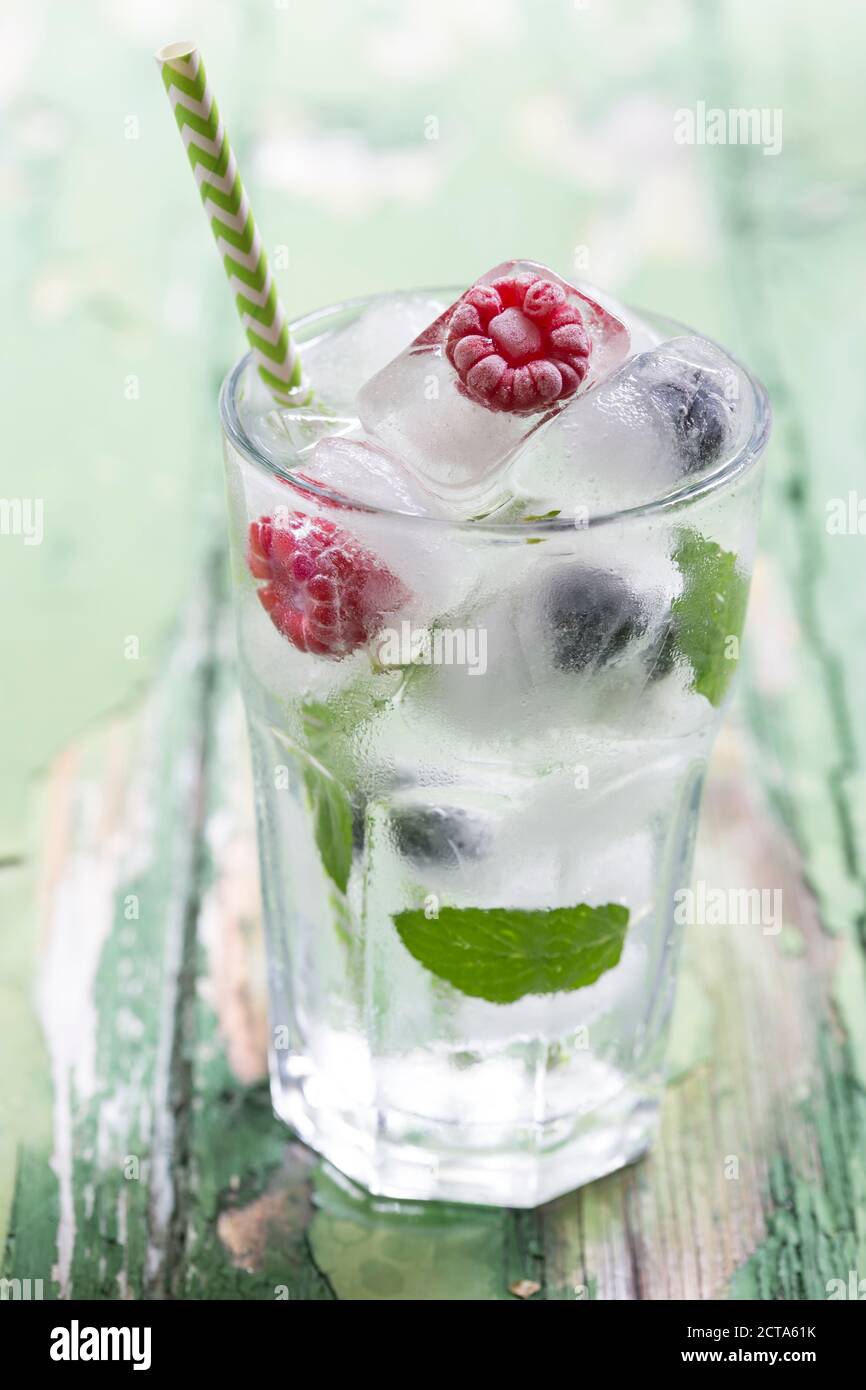 Glass of berries in ice cubes with mint leaves on wooden table, close up Stock Photo