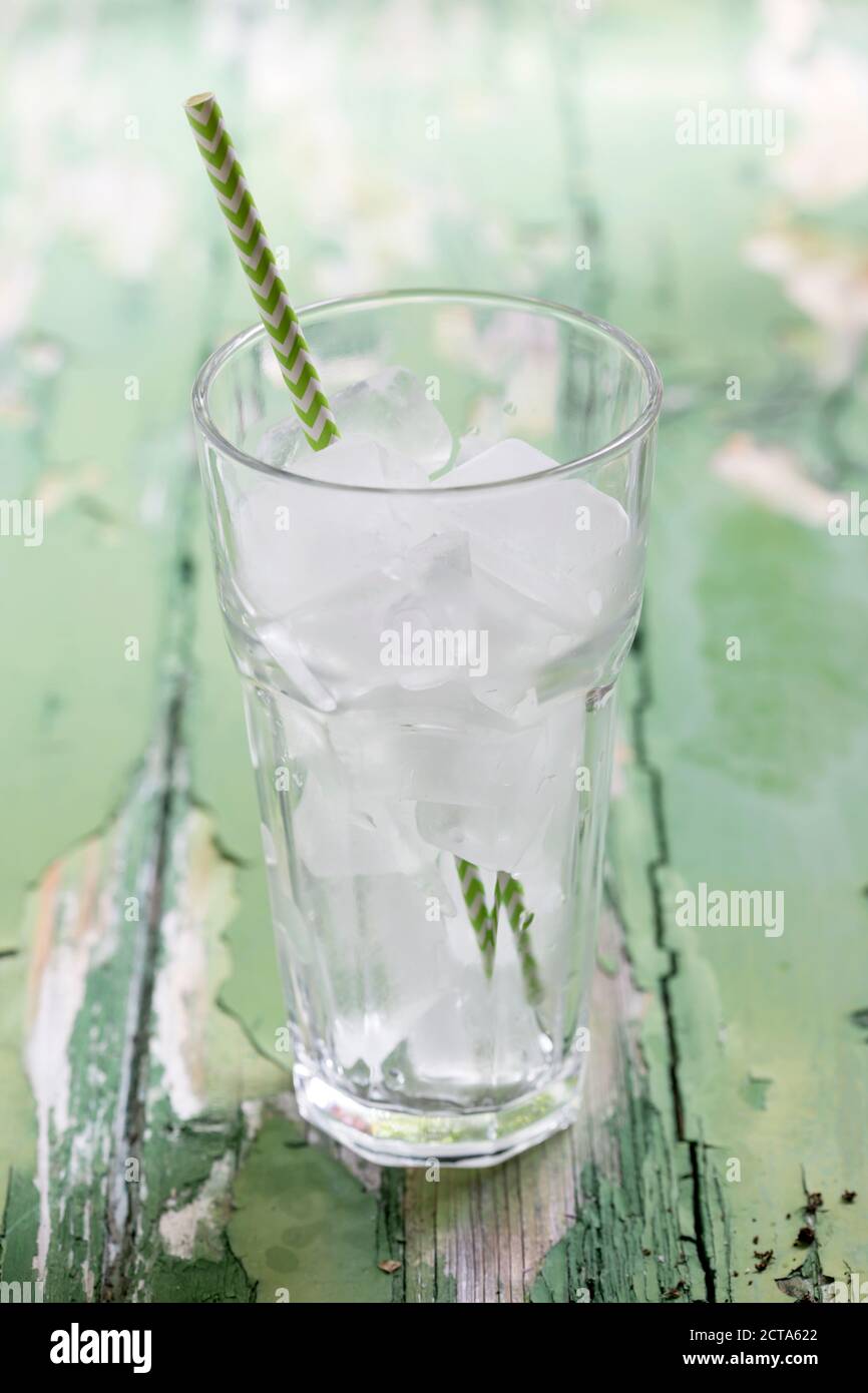 Glass of ice cubes with drinking straw on wooden table, close up Stock Photo