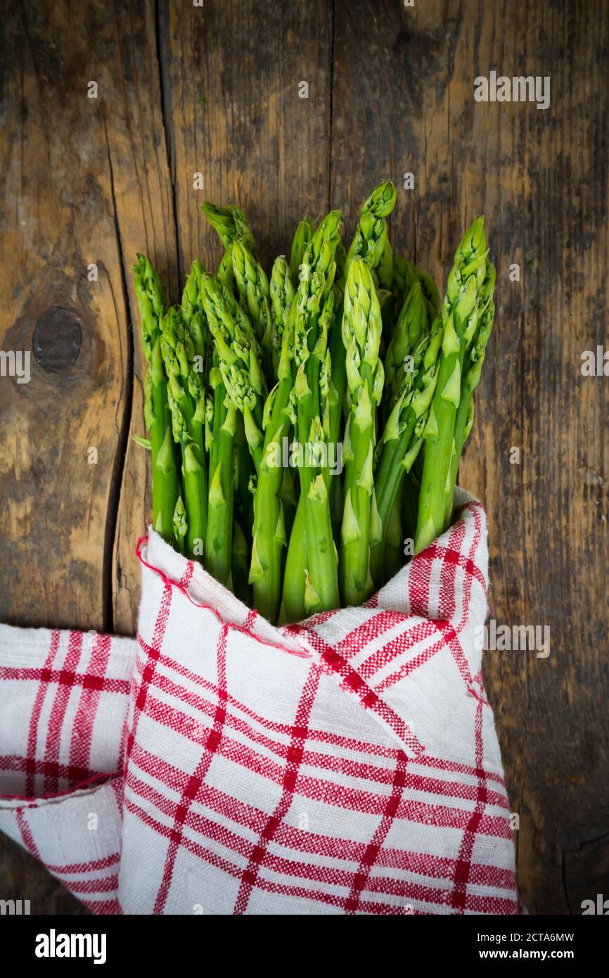 Bunch of green asparagus, Asparagus officinalis, wrapped in kitchen towel lying on dark wood Stock Photo