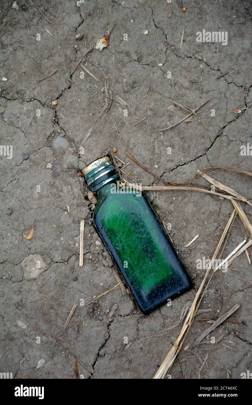 Green glass bottle trodden in soil, elevated view Stock Photo