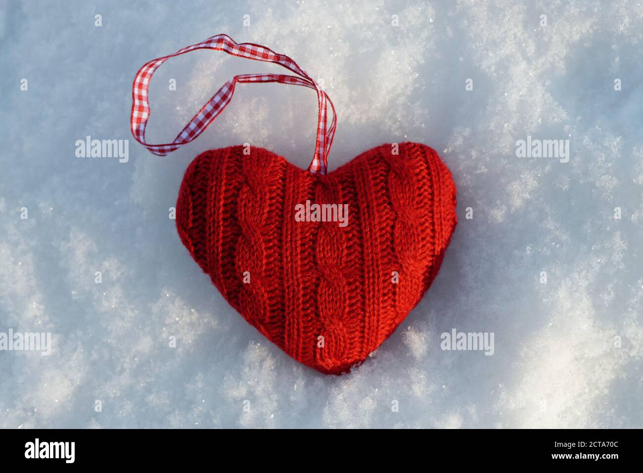 Red knitted heart lying on snow, close-up Stock Photo
