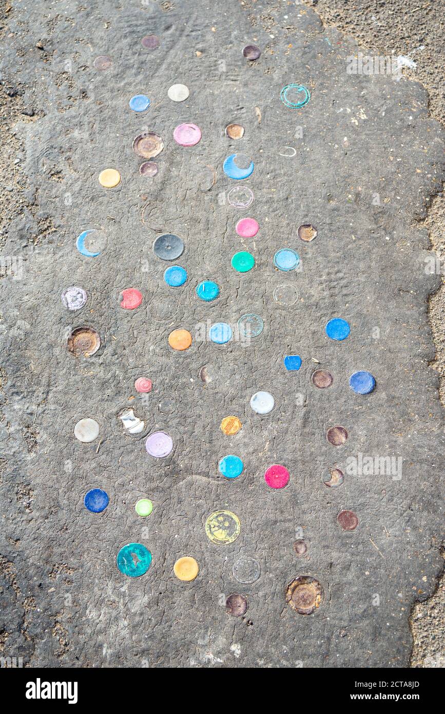 Plastic bottle tops pushed into tar layer of seawall in Chalkwell, Southend on Sea, Essex, UK. Cinder path on Thames Estuary with bottle caps Stock Photo