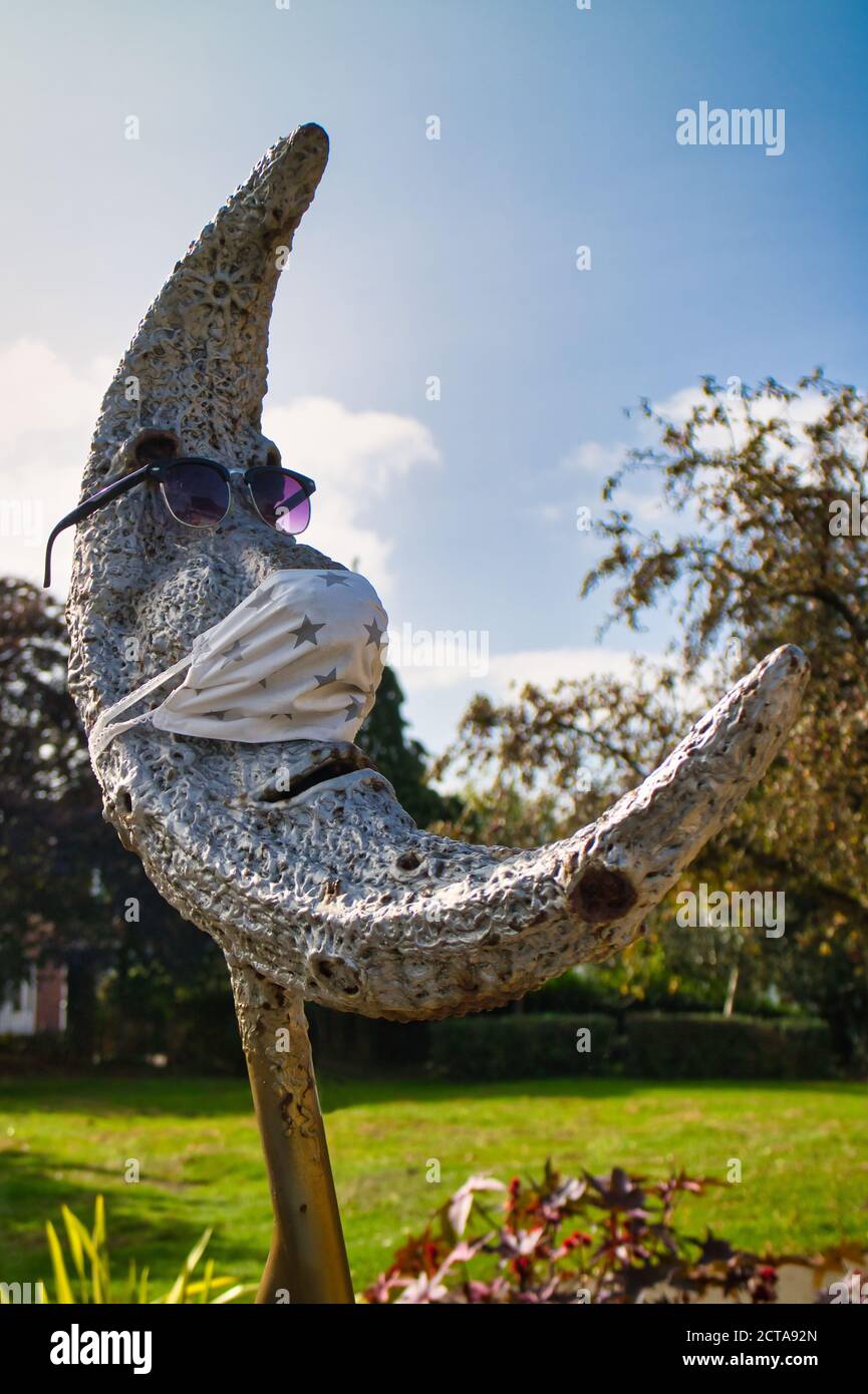 Park Statue of a moon has face mask (ppe) added to protect it from covid whilst looking cool in a pair of purple tinted sunglasses. Hinckley Leics. Stock Photo