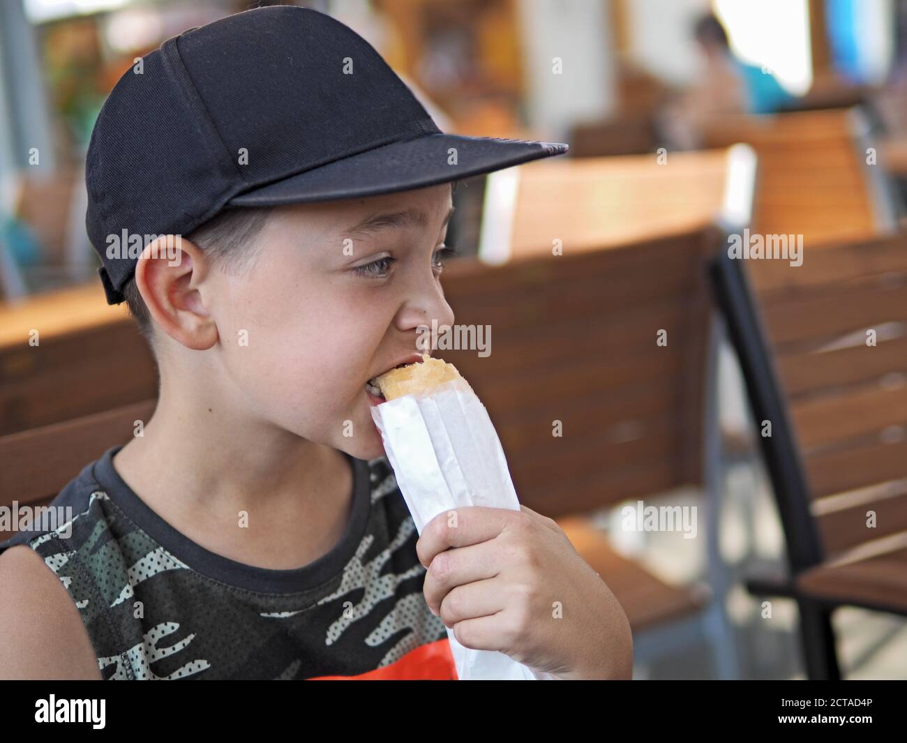 Young boy eats a hot dog at outdoor restaurant Stock Photo