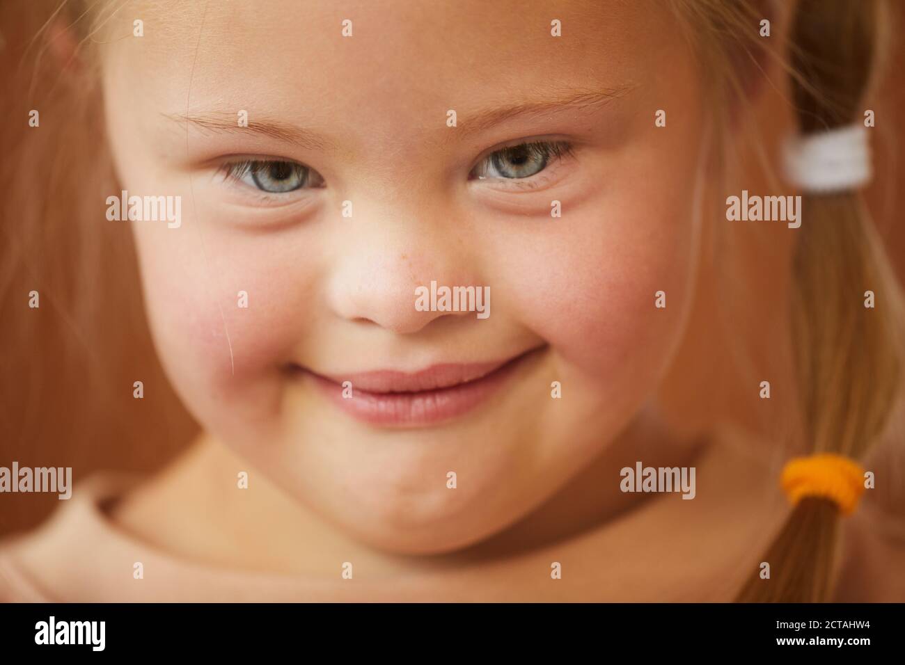 Close up portrait of cute girl with down syndrome smiling at camera happily, studio shot Stock Photo