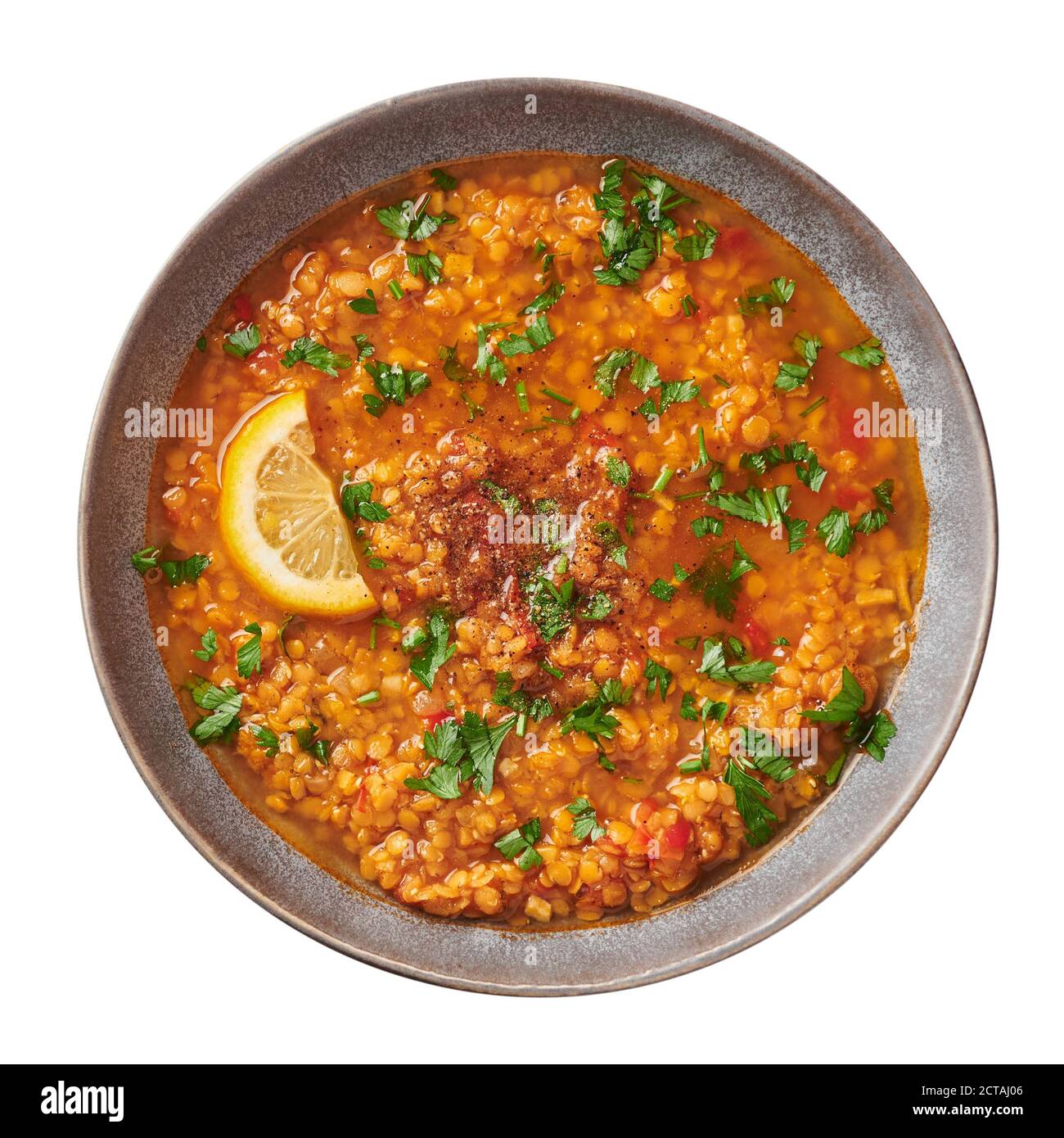 Red lentils tomato soup with parsley and lemon in gray plate isolated on white backdrop. Vegetarian dish. Stock Photo