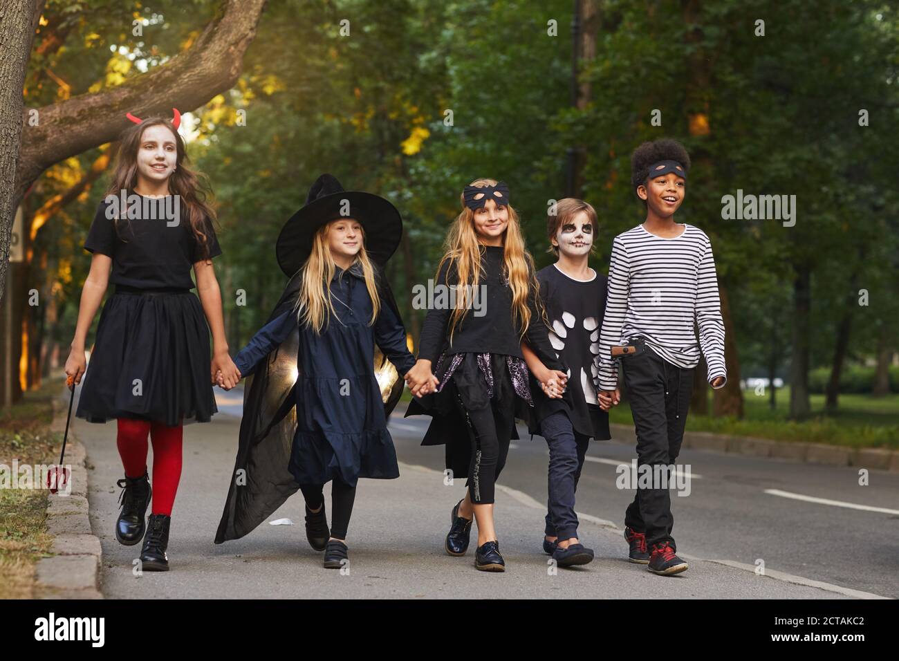 Full length portrait of multi-ethnic group of kids walking in street while trick or treating on Halloween Stock Photo