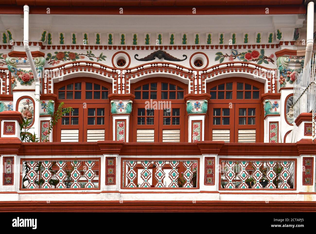 Restored Chinese peranakan shop house with brown wooden louvred shutters and ornately decorated ballustrades on the balcony. Stock Photo