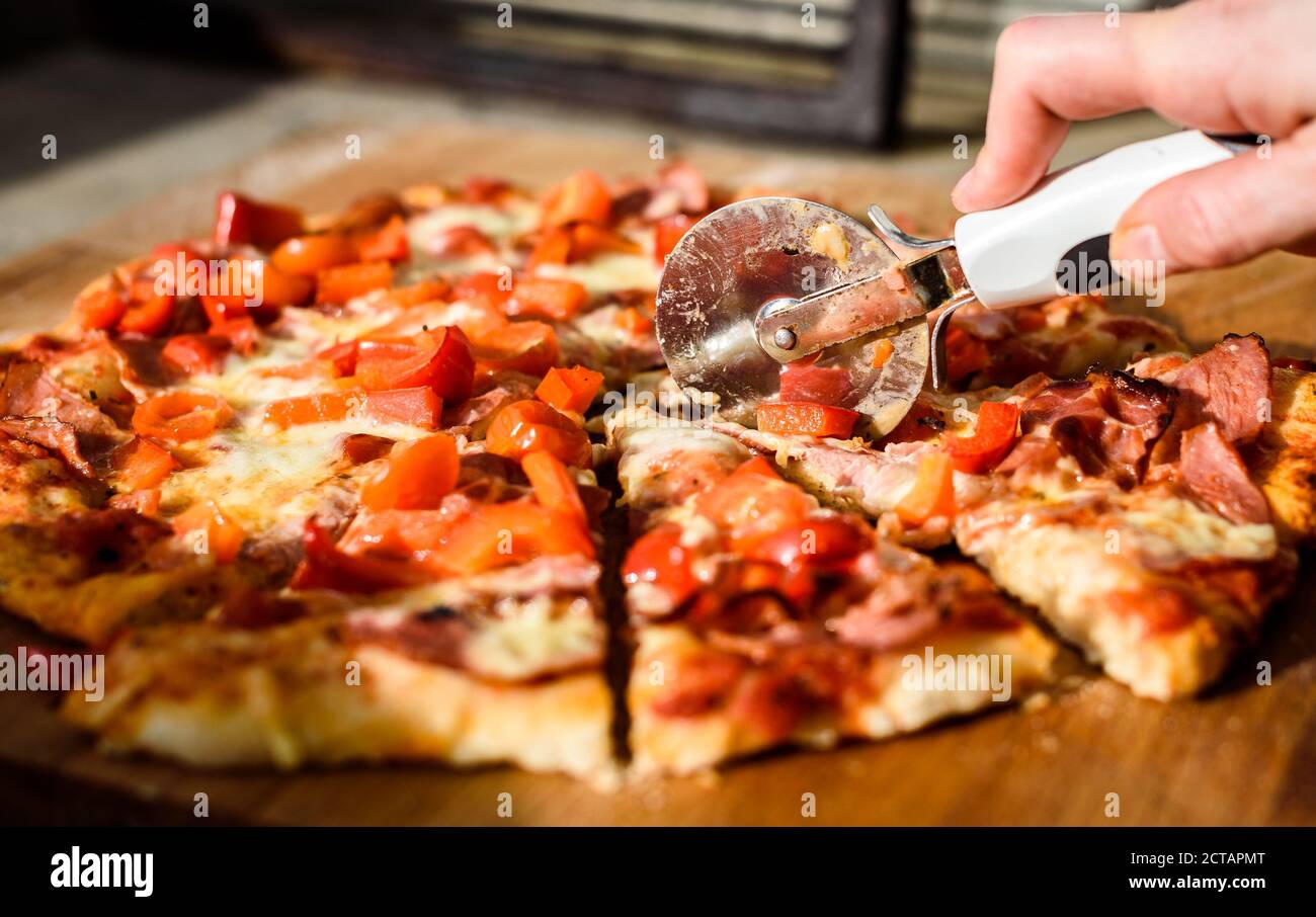 Making of homemade Italian pizza in fireplace brick oven. Making of traditional pizza in stone brick fireplace with fire wood and coals. Cutting finis Stock Photo