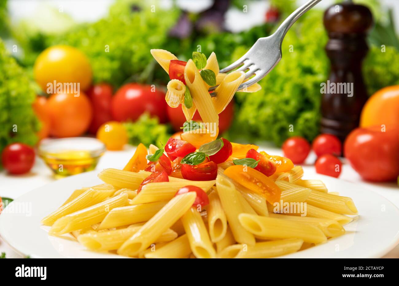 Plate of italian pasta, penne rigate on fork with tomatoes and basil Stock Photo