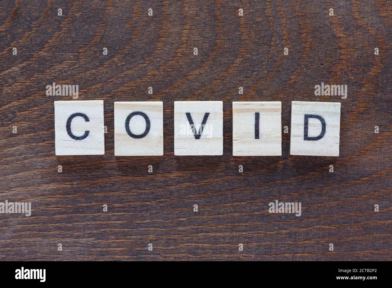 written 'COVID' with light wood letters on dark wood Stock Photo