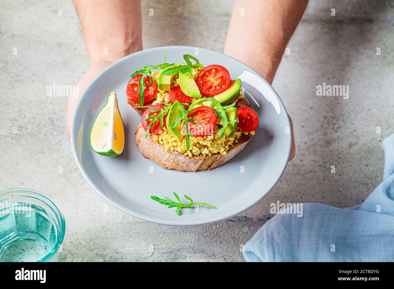 Tofu scrambled sandwich with avocado, arugula and tomato on a gray plate. Healthy vegan food concept. Stock Photo
