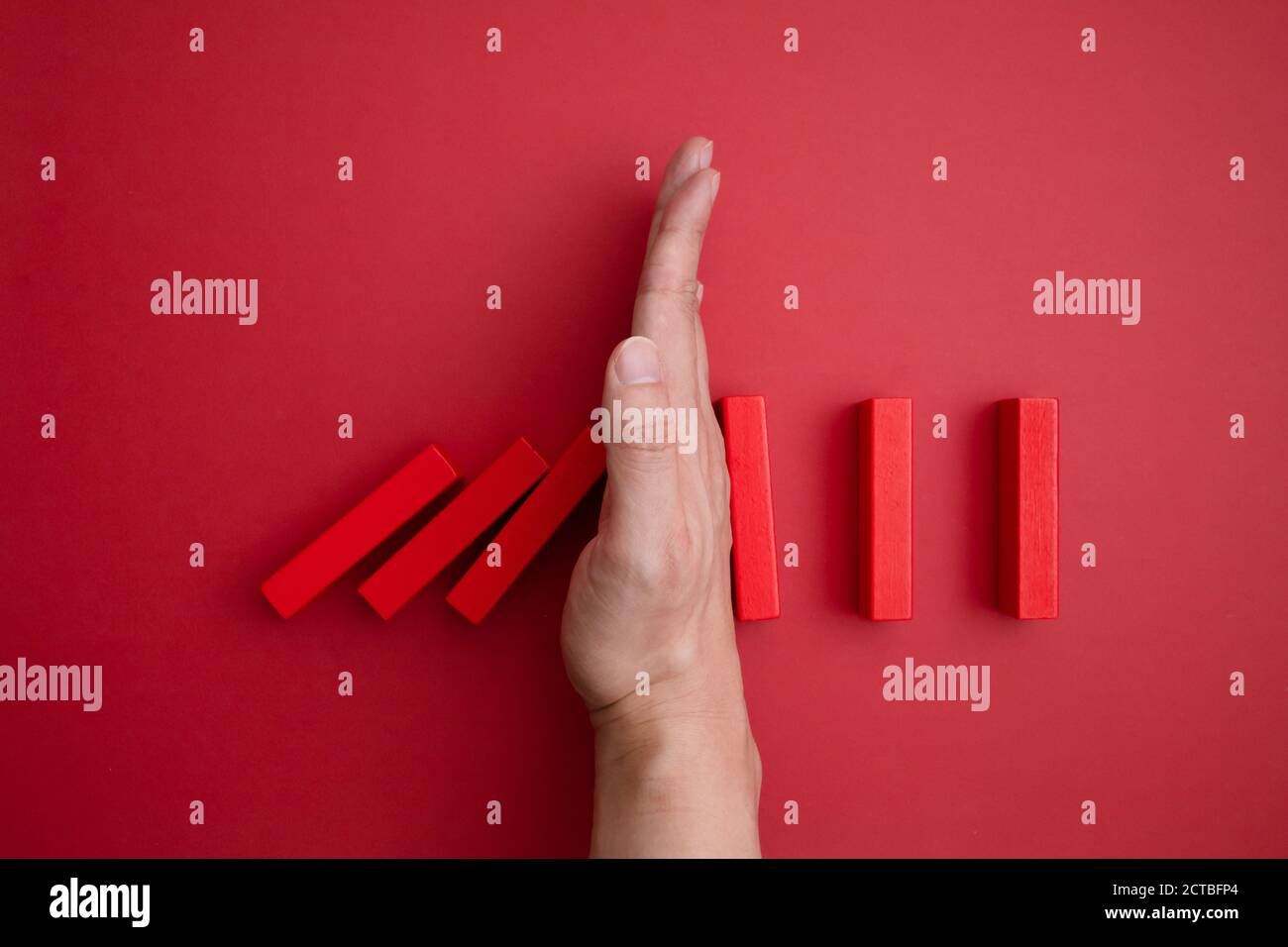 red domino blocks that begins to fall and a hand that prevents it from falling. Stock Photo