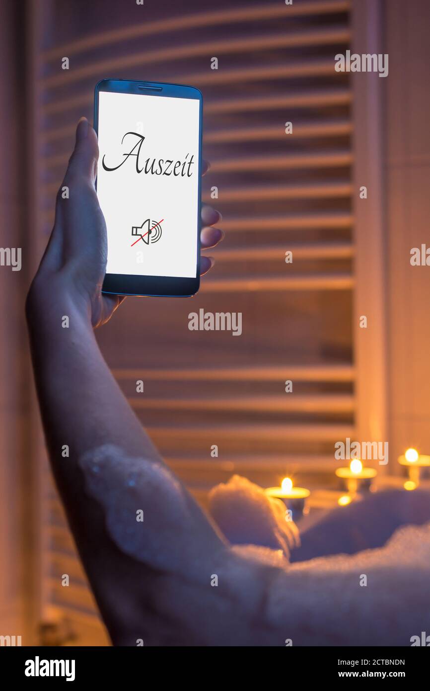 Woman bathes relaxed by candlelight in the tub and sounds of the phone with the German word time out in the display Stock Photo