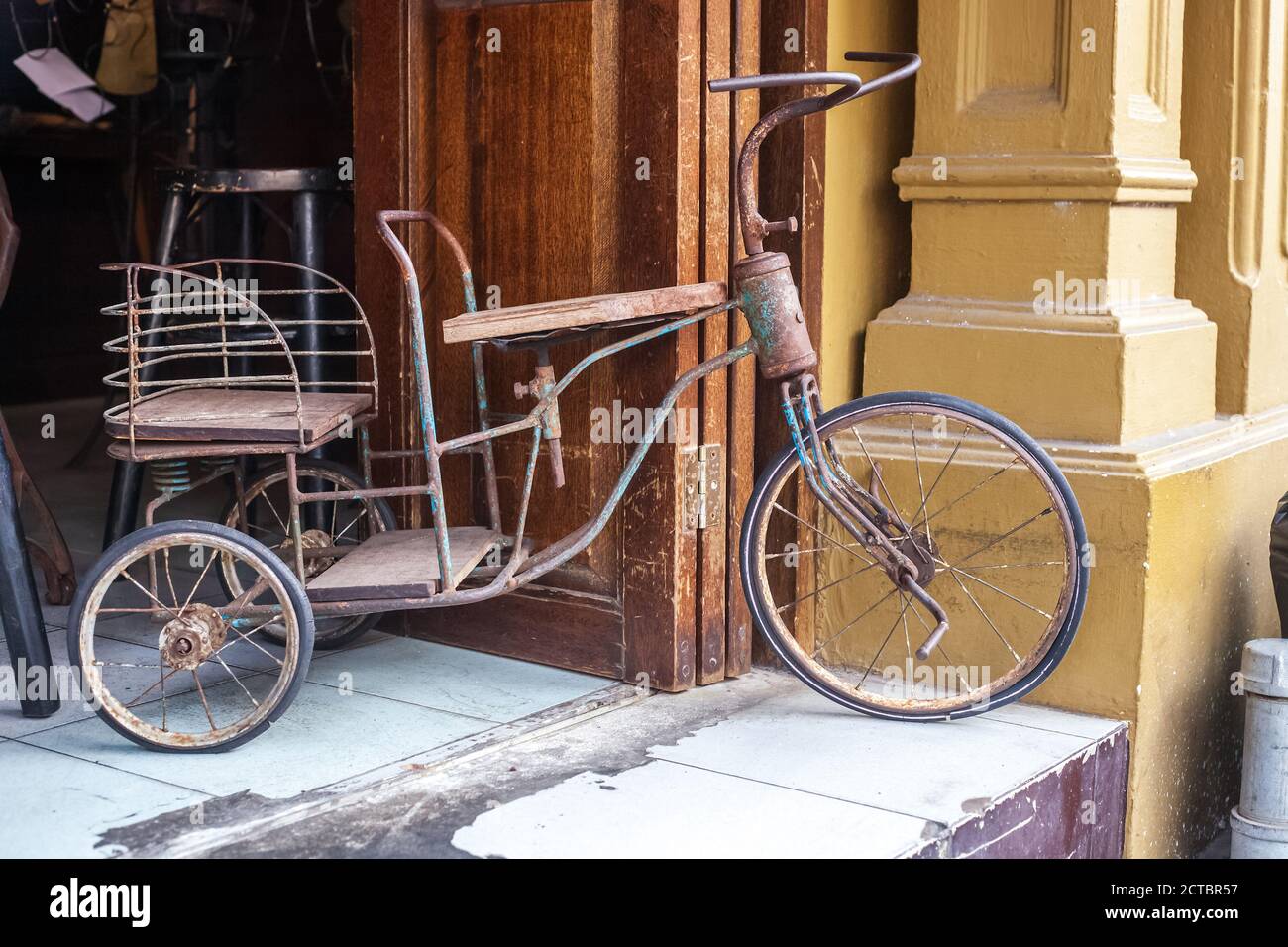 Old broken tricycle near house in Thailand. Vintage metal three-wheeled  bicycle standing on doorstep Stock Photo - Alamy