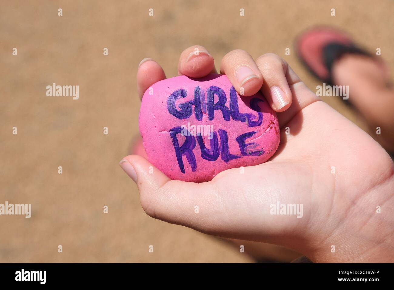 A child is holding a painted pink rock that says girls rule in purple letters for a self esteem girl power concept. Stock Photo