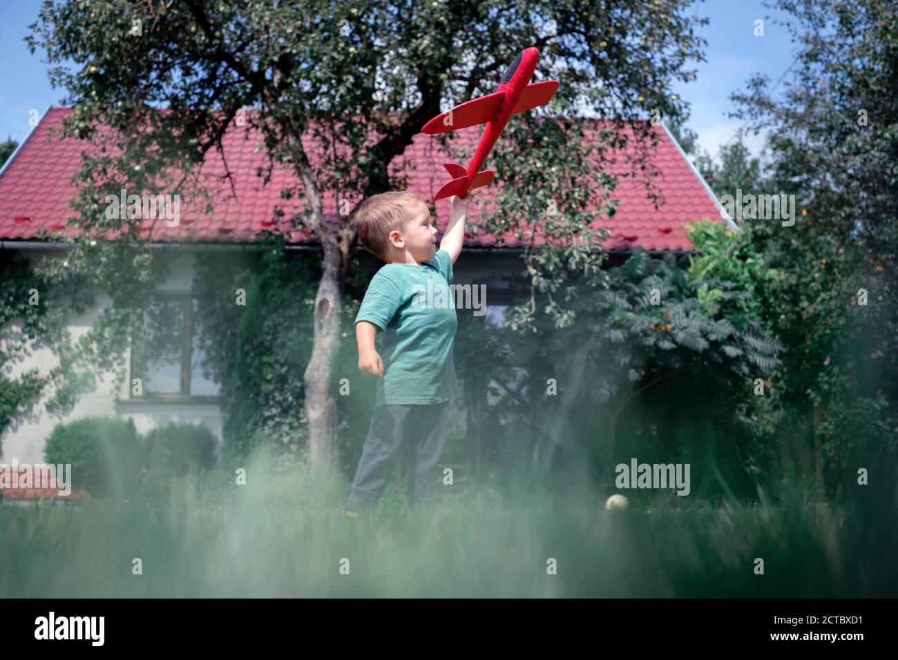 Happy kid playing with red airplane on lawn near his home Stock Photo