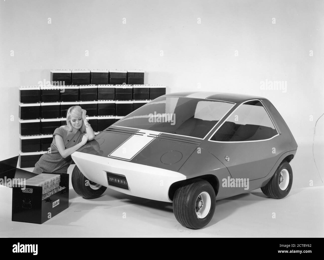 Publicity Photo for the Amitron, the American Motors Corporation and Gulton Industries electronic car powered by Gulton's long-life, light-weight lithium battery system. The AM prototype vehicle seen here is a  three-passenger car designed for short-haul transportation needs. The case in the foreground contains one-half of the lithium system, which is the equivalent in power to the 45 conventional automotive batteries, shown in the background, Detroit, MI, 1968. (Photo by RBM Vintage Images) Stock Photo