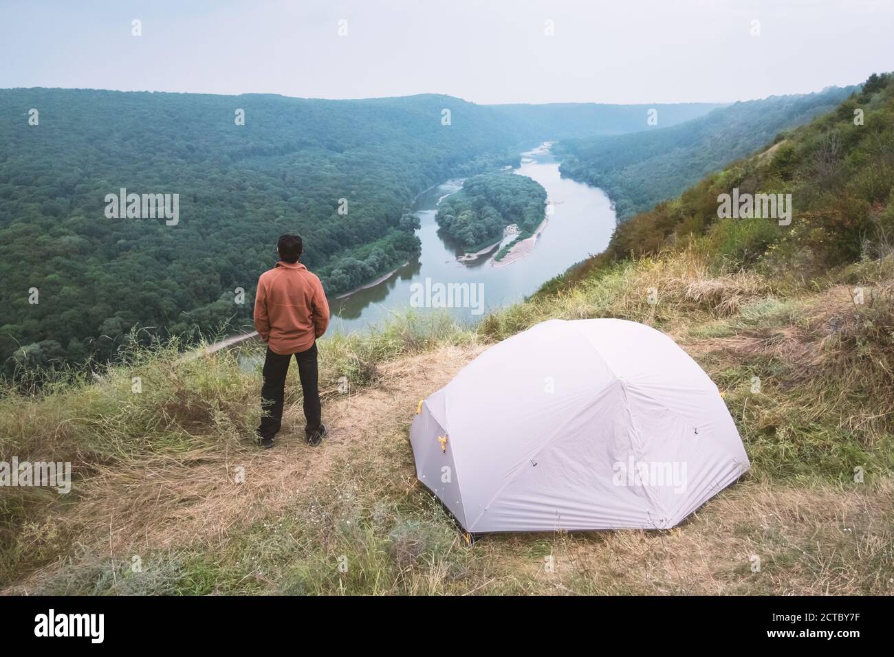 A tourist stands near a tent on the top of a mountain above the majestic Dniester River in Ukraine. Landscape photography Stock Photo