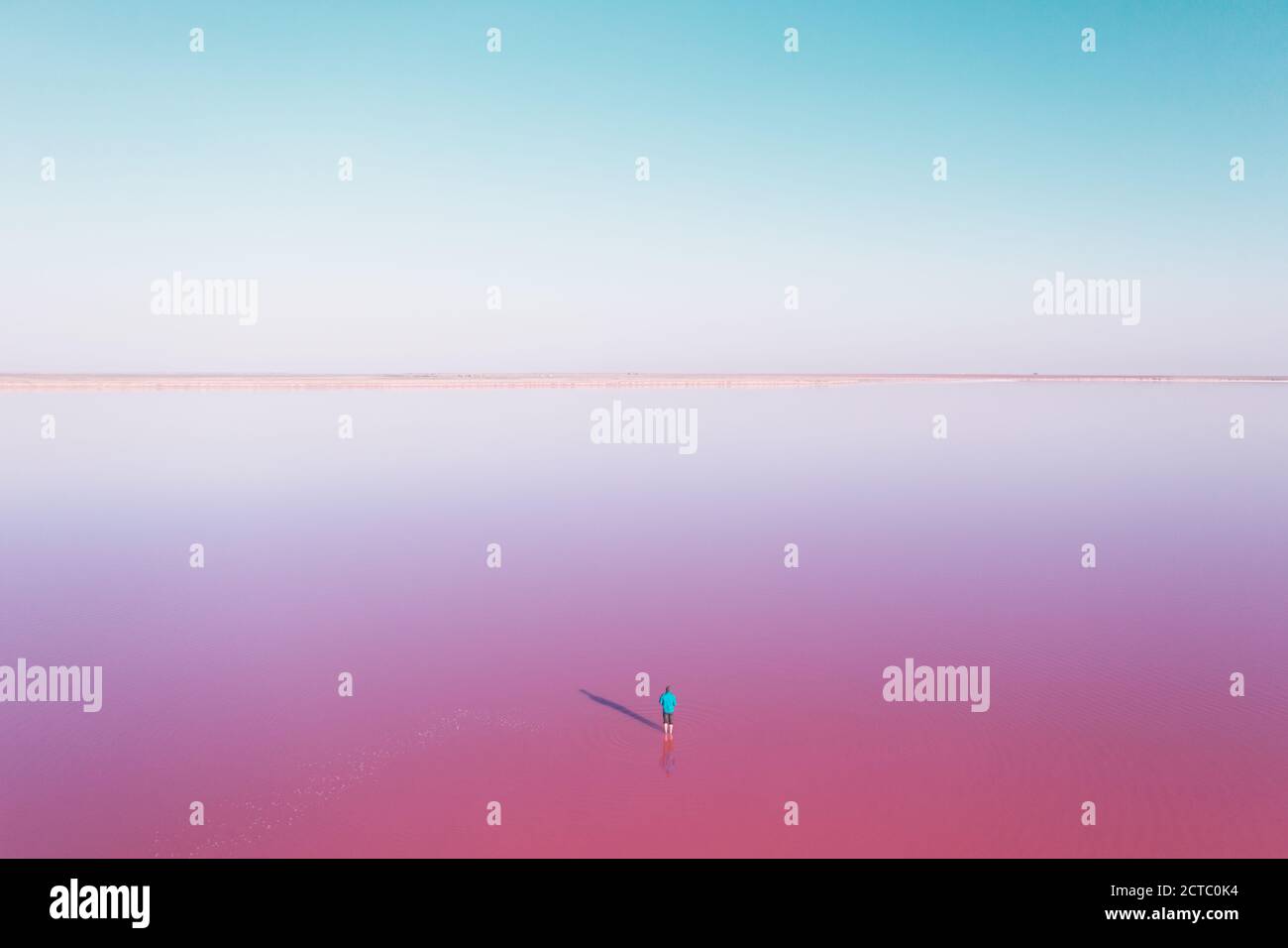 Lonely man in blue jacked in pink lake water under clear blue sky in summer day. Creative color concept Stock Photo