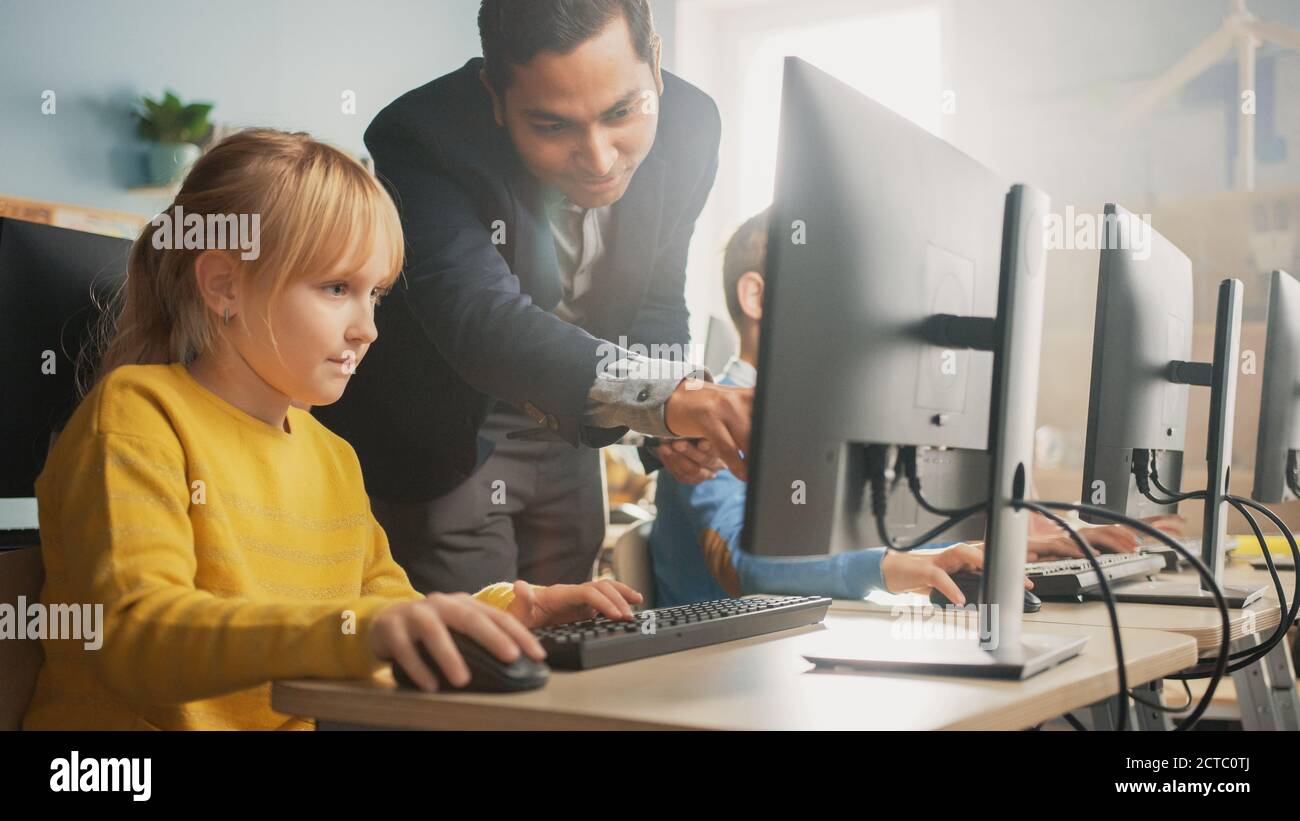 Elementary School Science Classroom: Teacher Explains to a Smart Little Schoolgirl how to use Personal Computer, to Learn Programming Language needed Stock Photo
