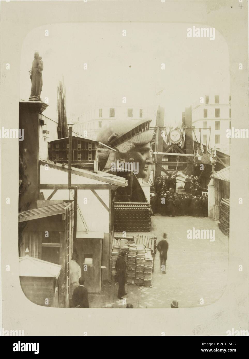 View of the external area of the workshop in Paris, showing construction materials, the head of the Statue of Liberty, and a group of men gathered in front of the left foot of the statue., still image, Photographs, 1883, Fernique, Albert, 1841-1898 Stock Photo