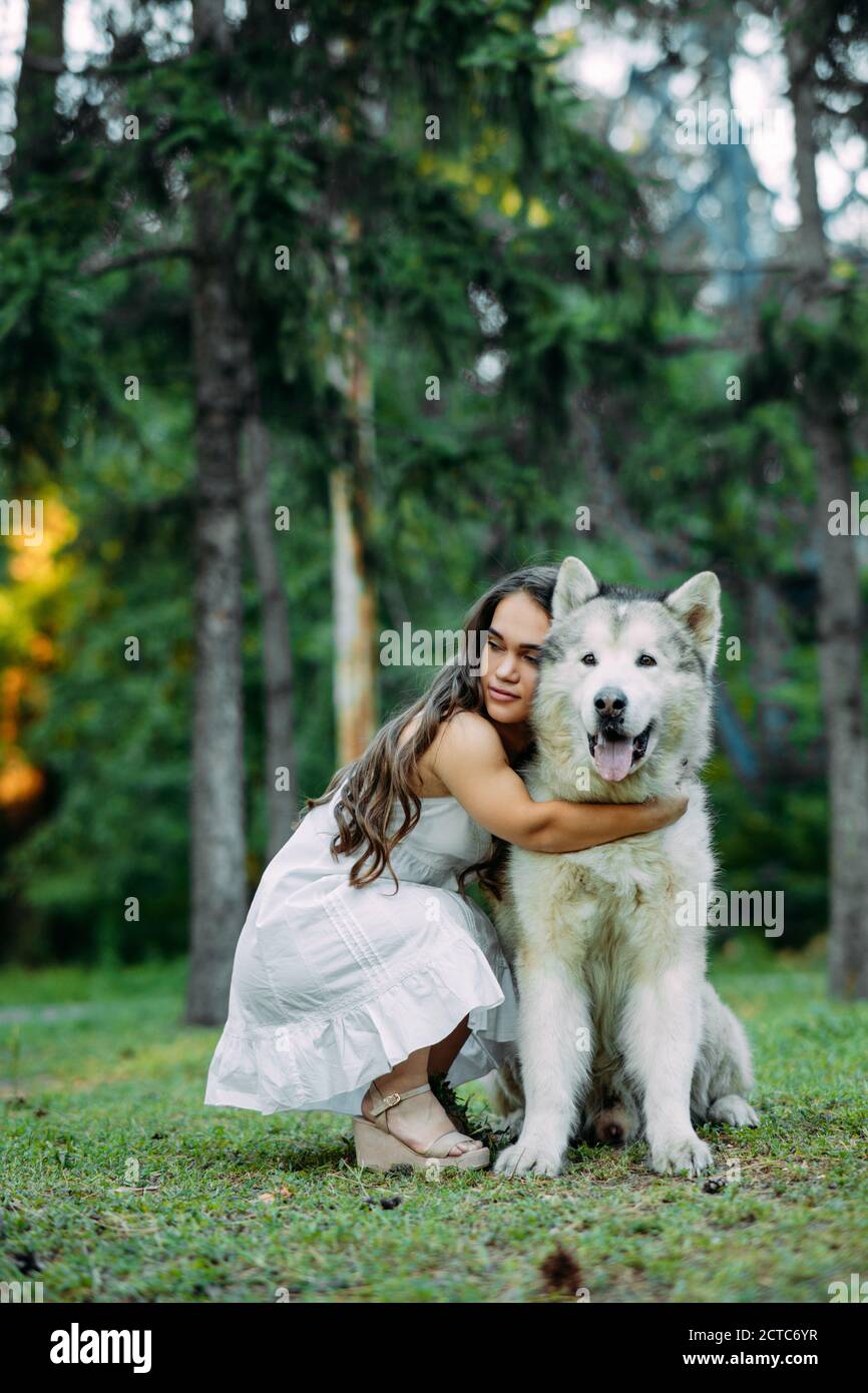 Young woman with innate disorder dwarfism embraces Malamute dog while walking in park. Stock Photo