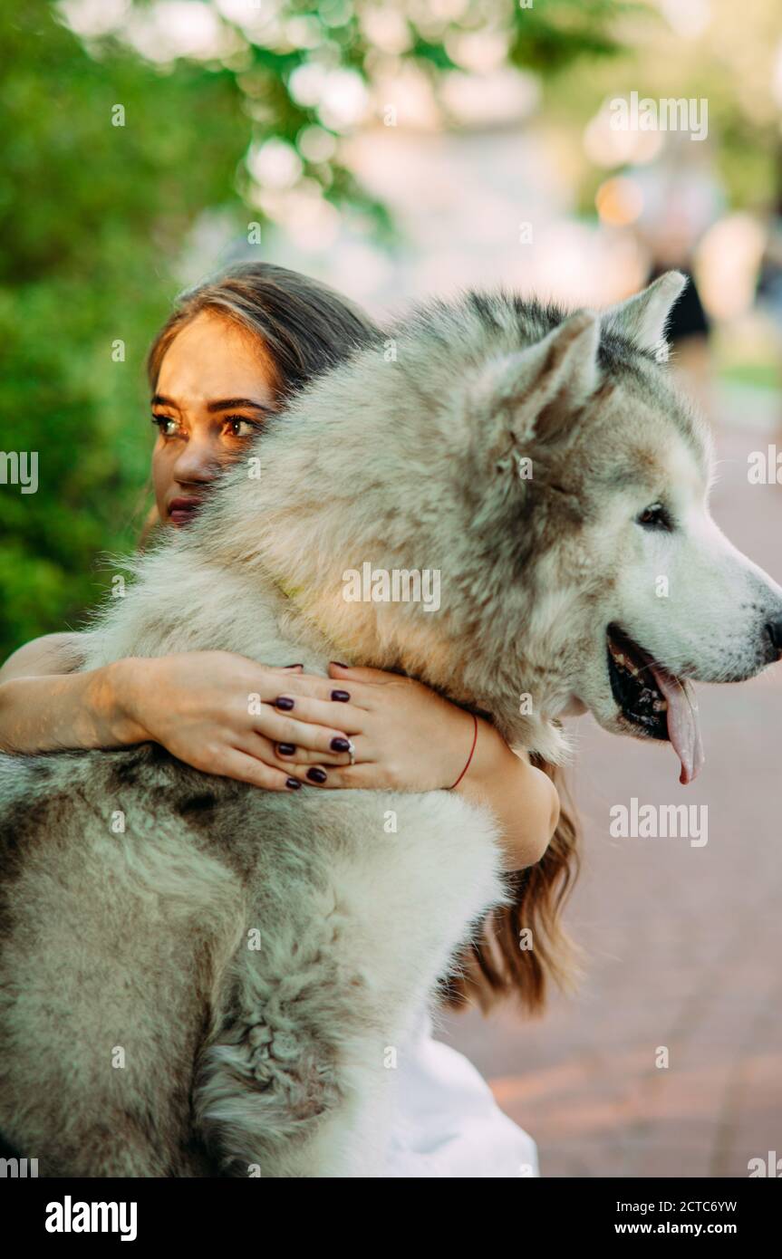 Young woman with innate disorder dwarfism embraces Malamute dog while walking in park. Stock Photo